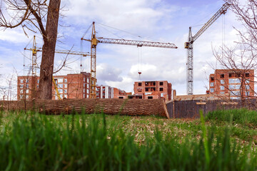 Fototapeta na wymiar Multi-storey brick houses under construction. Lawn of green grass on the background of the construction site.