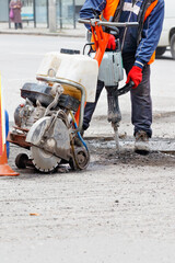 A road worker repairs a section of road with an electric jackhammer and gas cutter.