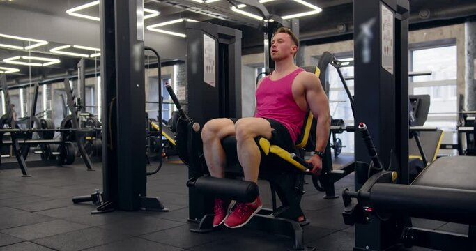 A young man trains his legs in a leg trainer. Pumps the quadriceps.