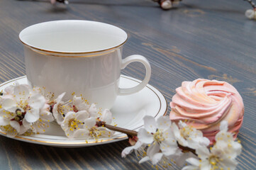 white porcelain cup with white and pink marshmallows and blooming apricot branch on a wooden table