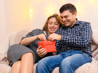 portrait of adult romantic couple sitting on a couch at home, holiday lights on a wall