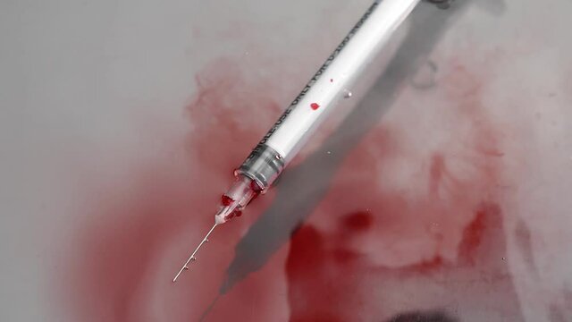 White syringe with blood falls on the white floor
