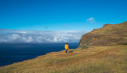 Young female dressed in orange waterproof jacket walking by the mountain above the cloud route on...