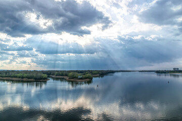  Light of the setting sun through the clouds. River and sky