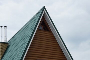 brown wooden attic of a private house with a small window under a green tiled roof against a gray sky