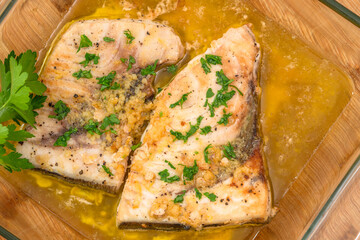 Swordfish stakes with lemon butter sauce and parsley. Two fish stakes close up in a glass bowl directly from above