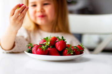 Cute little girl eating fresh strawberry in the kitchen. Healthy vitamin snack for kids. Ripe fresh berries. Harvest season. Natural vitamins .