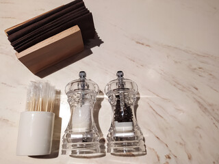 Salt and pepper in glass salt shakes, holder with napkins on a marble table. View from above