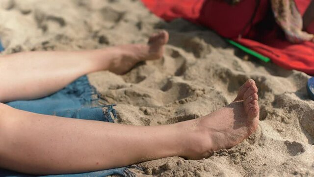 Young woman sunbathing on the beach, detail to her feet, toe wiggling as she tries to get sand off