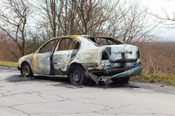 Fototapeta na wymiar Burned car after an accident on the asphalt road. Side view. Arson of a car, criminal showdowns
