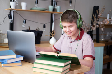 teenager boy in headphones studying online using laptop writing in notebook, reading book