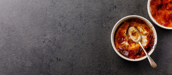 Creme brulee with cracked sugar crust and spoon on dark background copy space