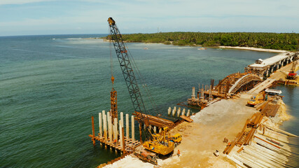 Pile driving machine in construction site.The bridge under construction across the bay and construction equipment with workers on the bridge. Siargao, Philippines.