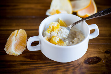 cooked boiled sweet oatmeal with oranges in a bowl