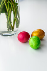 Vase with flowers and Easter eggs on a white table.