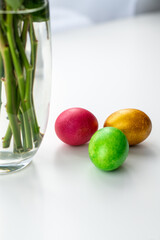 Vase with flowers and Easter eggs on a white table.