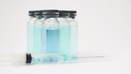 Vial vaccine, glass ampoules with transparent and blue liquid, a syringe is lying near on white background, global vaccination concept