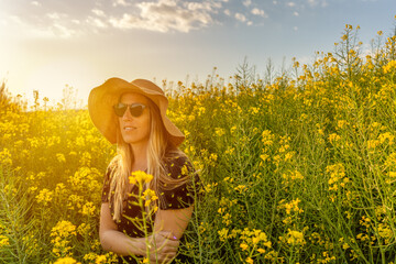 Naklejka na ściany i meble Woman in straw sun hat enjoying spring in yellow flowers field.Summer concept lifestyle female against sunset golden light in nature .