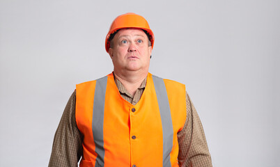 fat construction worker in funny confusion in helmet on grey background, bulder does not understand with humorous face expression