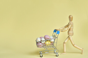 Wooden mannequin with shopping cart with colorful easter eggs on light background.Easter sale.business, shopping concept