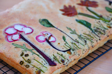 View of a focaccia bread decorated with a garden made of vegetables on top