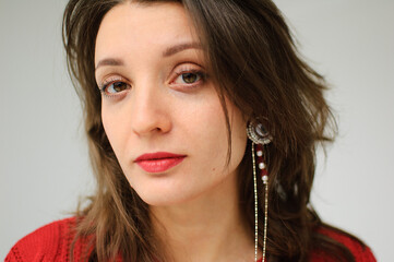 Studio portrait of young woman in red knitted sweater and earring on white background