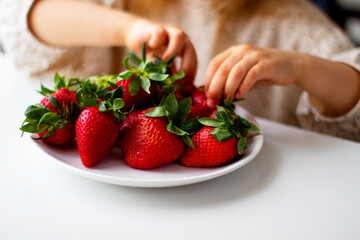  Cute little girl eating fresh strawberry in the kitchen. Healthy vitamin snack for kids. Ripe fresh berries. Harvest season. Natural vitamins .