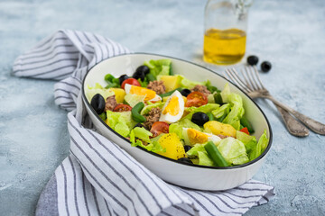 American version of Nicoise salad with canned tuna, boiled potatoes and green asparagus beans in an oval white dish on a gray concrete plate.