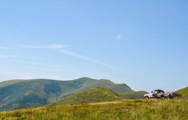 SUV and two motorcycles stands at peak of the hill with beautiful mountains at background. Adventure in the mountains, car travel off road.