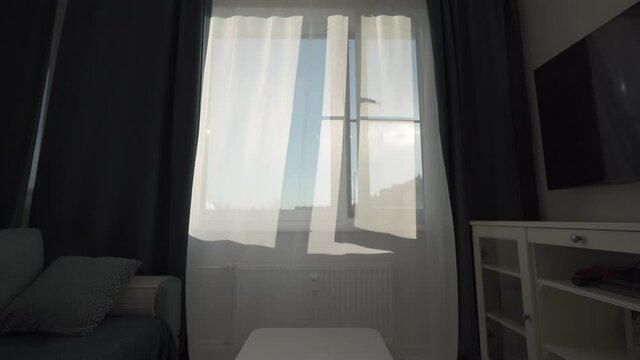 Transparent curtain on open window moved by the wind at sunny day, sun rays shine through the transparent tulle on window of apartment room. High quality 4k footage