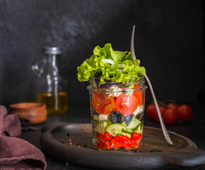 Healthy greek salad with fresh vegetables and feta cheese in a glass jar on a dark concrete background. Salad recipes.