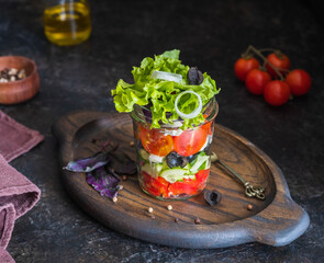 Healthy greek salad with fresh vegetables and feta cheese in a glass jar on a dark concrete background. Salad recipes.
