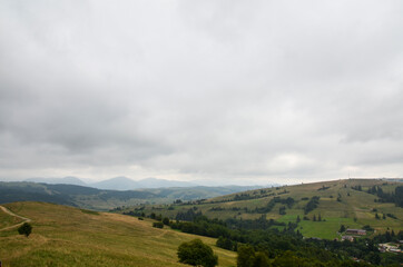 Carpathian mountains with green slopes under low in thick clouds and fog on a cloudy day. 