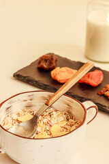 Muesli in white bowl, dried fruit on black cutting board and a bottle of milk on white background. Breakfast concept. Stock photo