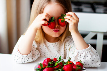  Cute little girl eating fresh strawberry in the kitchen. Healthy vitamin snack for kids. Ripe fresh berries. Harvest season. Natural vitamins .