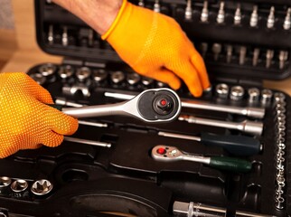 Male hand in building glove with socket ratchet handle taking from repair suitcase. Industrial...