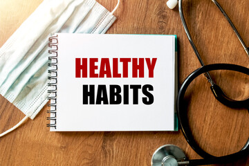 Inscription - HEALTHY HABITS. Written in a notepad to remind you of what's important. Top view of the table along with a stethoscope and a mask. Health care concept.