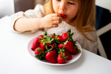 Cute little girl eating fresh strawberry in the kitchen. Healthy vitamin snack for kids. Ripe fresh berries. Harvest season. Natural vitamins .