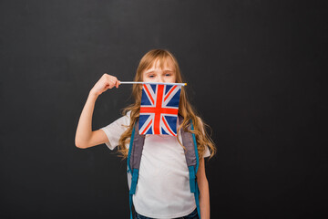 Happy child girl 8-9 y.o. holds a miniature of the English flag. Learn English Language. Education Concept.