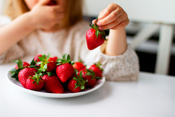Cute little girl eating fresh strawberry in the kitchen. Healthy vitamin snack for kids. Ripe fresh berries. Harvest season. Natural vitamins .