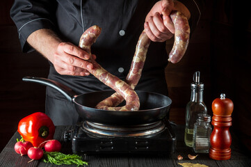 The cook puts raw meat sausage into the pan before cooking. Working environment in restaurant kitchen with vegetables and spices on the vintage table