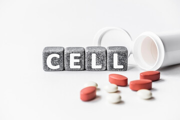 word CELL is made of stone cubes on a white background with pills. medical concept of treatment, prevention and side effects. basic building block of all living organisms