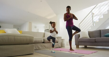 Happy african american mother and daughter doing yoga exercise at home - Powered by Adobe
