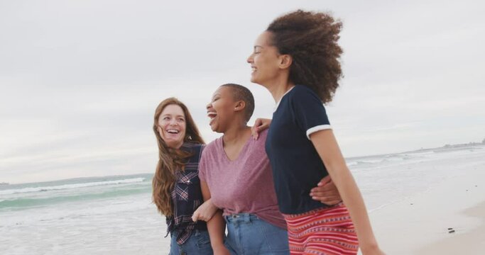 Diverse group of happy female friends walking on the beach embracing