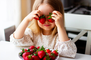 Cute little girl eating fresh strawberry in the kitchen. Healthy vitamin snack for kids. Ripe fresh berries. Harvest season. Natural vitamins .