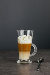 Tall glass cappuccino mug sits on a stone countertop against a dark background. Copy space.