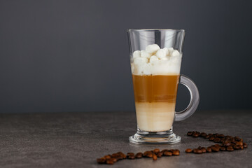 Tall glass cappuccino mug sits on a stone countertop against a dark background. Copy space.