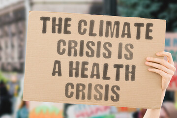 The phrase " The climate crisis is a health crisis " on a banner in men's hand with blurred background. Responsibility. Sick. Sickness. Temperature. Sustainable environment. Treatment. Ecological.