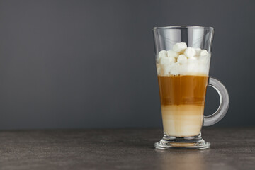 Tall glass cappuccino mug sits on a stone countertop against a dark background. Copy space.
