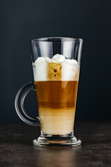 Tall glass cappuccino mug sits on a stone countertop against a dark background. Copy space.